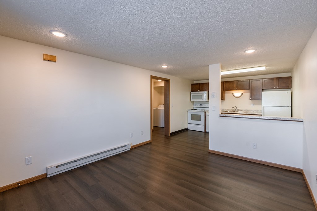 an empty living room and kitchen with white walls and wood flooring. Fargo, ND Berkshire Apartments