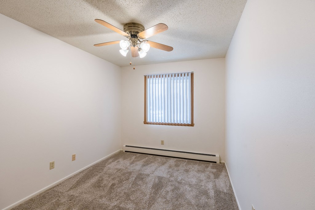 a bedroom with a ceiling fan and carpet. Fargo, ND Betty Ann Apartments