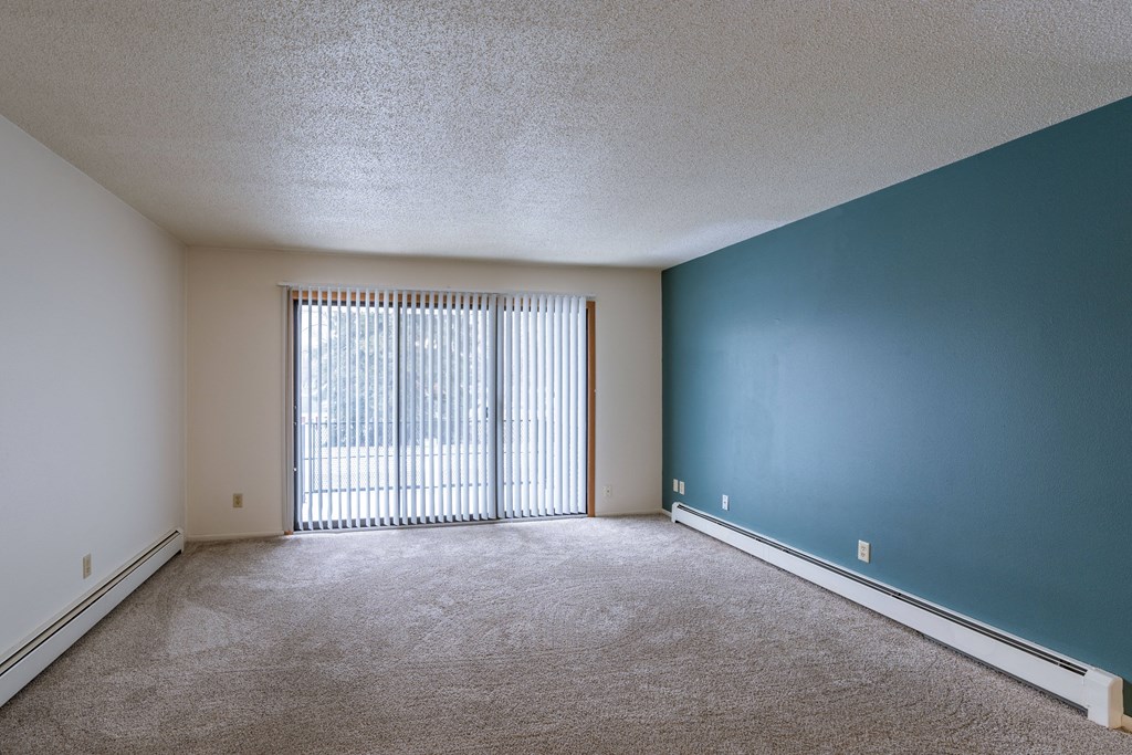 an empty living room with a large window and a blue wall. Fargo, ND Betty Ann Apartments