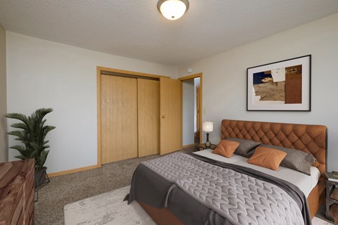 a bedroom with a large bed and a potted plant. Fargo, ND Birchwood 2 Apartments