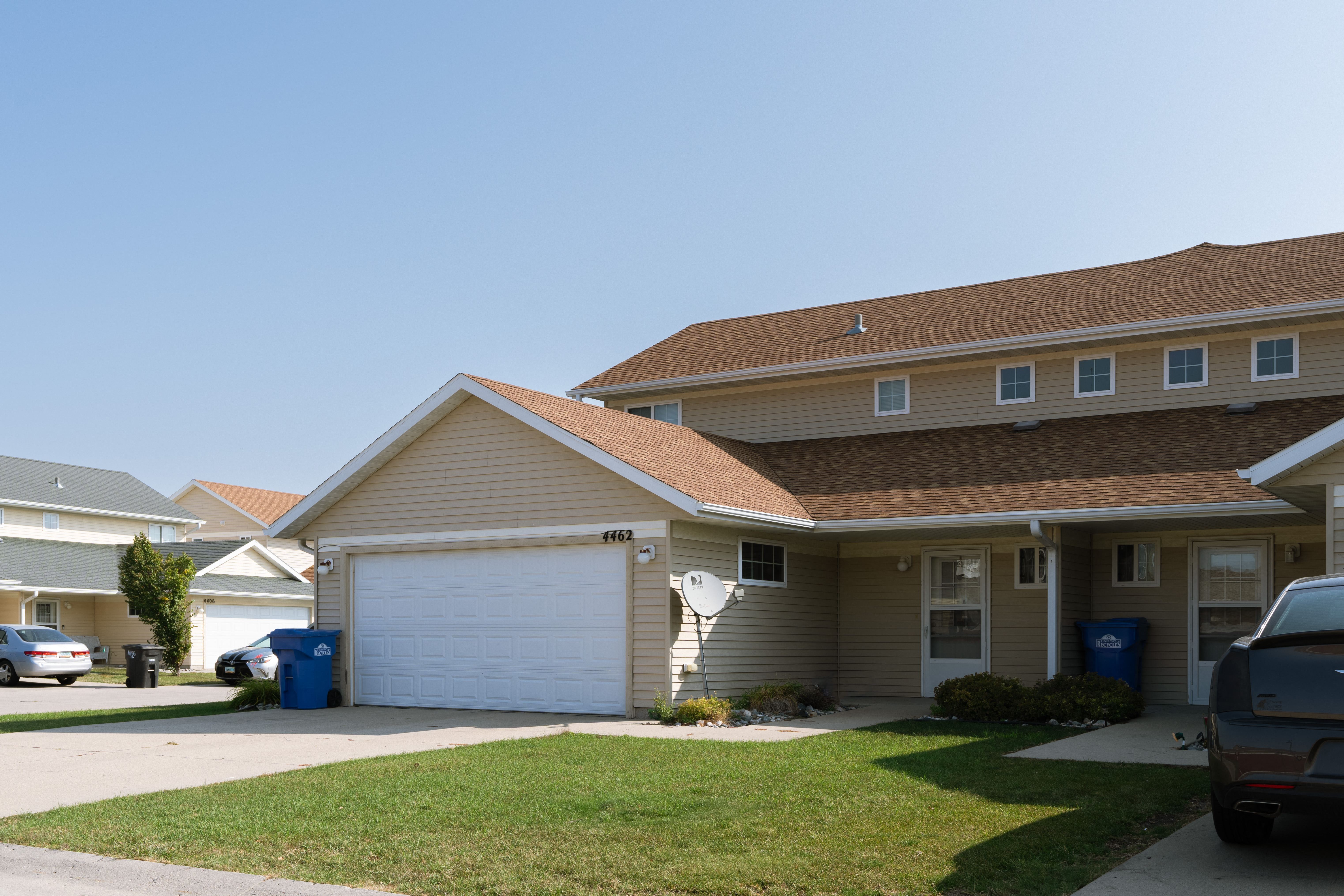 a tan house with a white garage door and a lawn. Fargo, ND Bluestem Townhome
