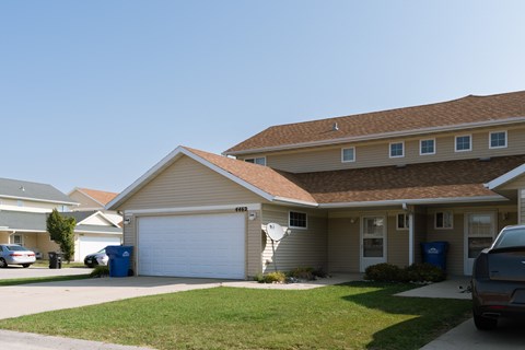 a tan house with a white garage door and a lawn. Fargo, ND Bluestem Townhome