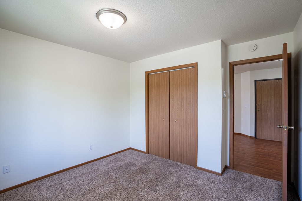 a bedroom with a door to a closet and a carpeted floor. Fargo, ND Briar Pointe Apartments
