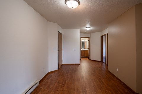 an empty living room and hallway with wood floors and white walls. Fargo, ND Briar Pointe Apartments