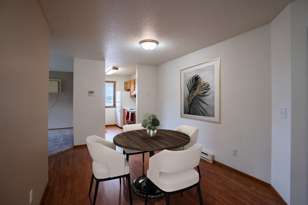 a dining room area with a table and chairs and a living room in the background. Fargo, ND Briar Pointe Apartments