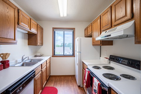 a kitchen with white appliances and wooden cabinets and a window. Fargo, ND Briar Pointe Apartments