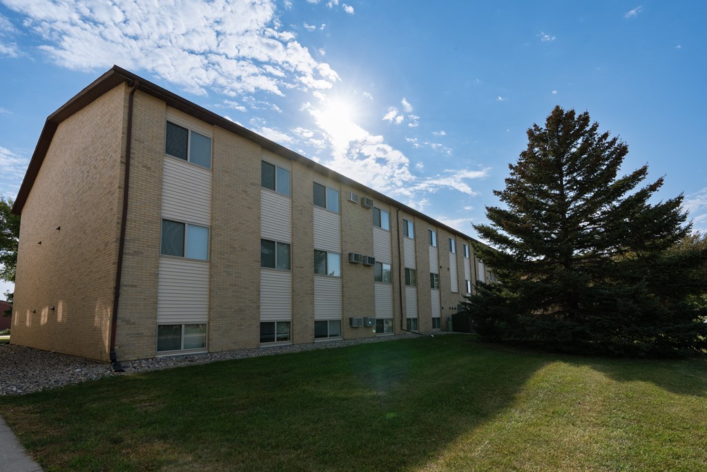 the exterior of a brick building with a green lawn and a tree. Fargo, ND Brookfield Apartments