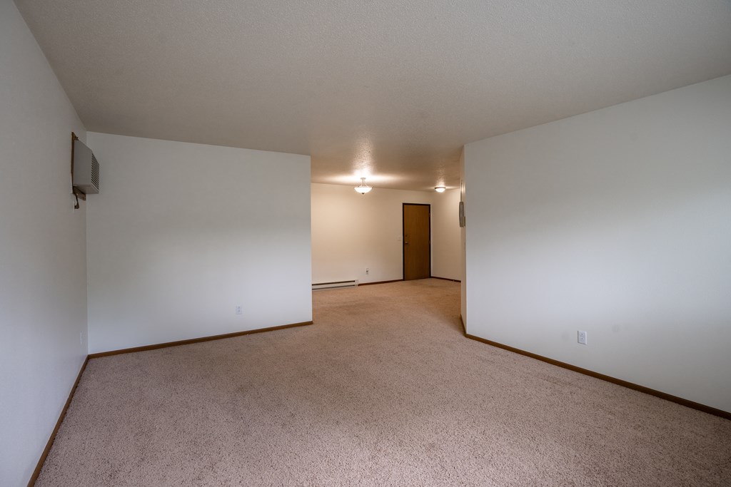 the living room and dining room of an apartment with white walls and carpet. Fargo, ND Brownstone Apartments