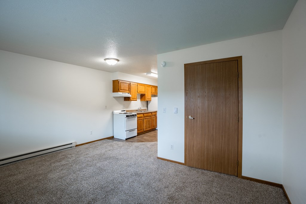 an empty living room with a door to a kitchen. Fargo, ND Brownstone Apartments