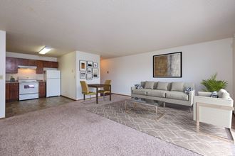 Fargo, ND Carlton Place Apartments. a living room with a couch a table and a chair and a kitchen with a stove and