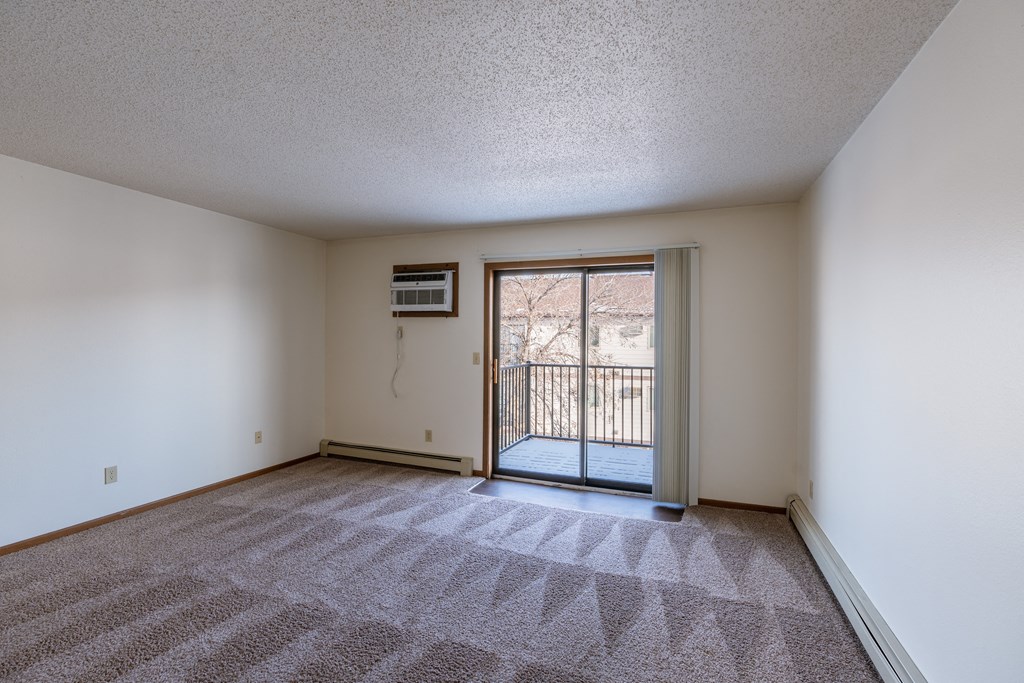 an empty living room with a door to a balcony. Fargo, ND Carlton Place Apartments