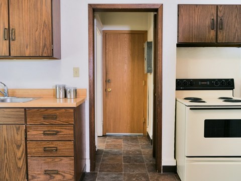 a kitchen with white appliances and wooden cabinets and a door to a hallway