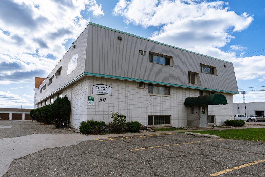 a white building with a green roof and a parking lot. Fargo, ND Cityside Apartments