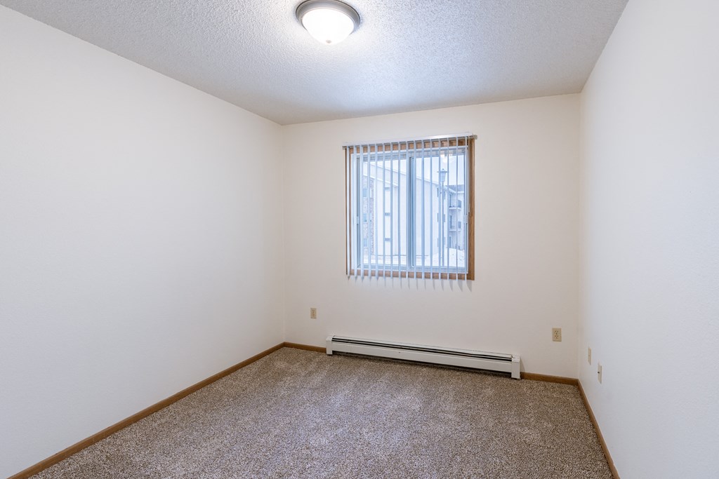 a spacious bedroom with carpet and a window. Fargo, ND Country Edge Apartments
