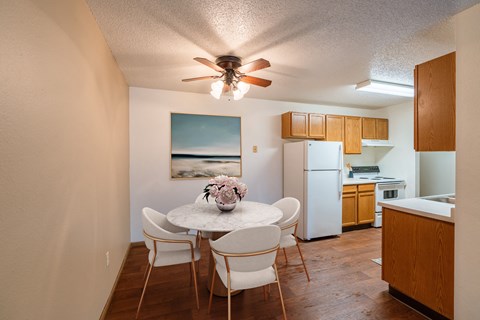 a dining area with a table and chairs and a kitchen with a refrigerator