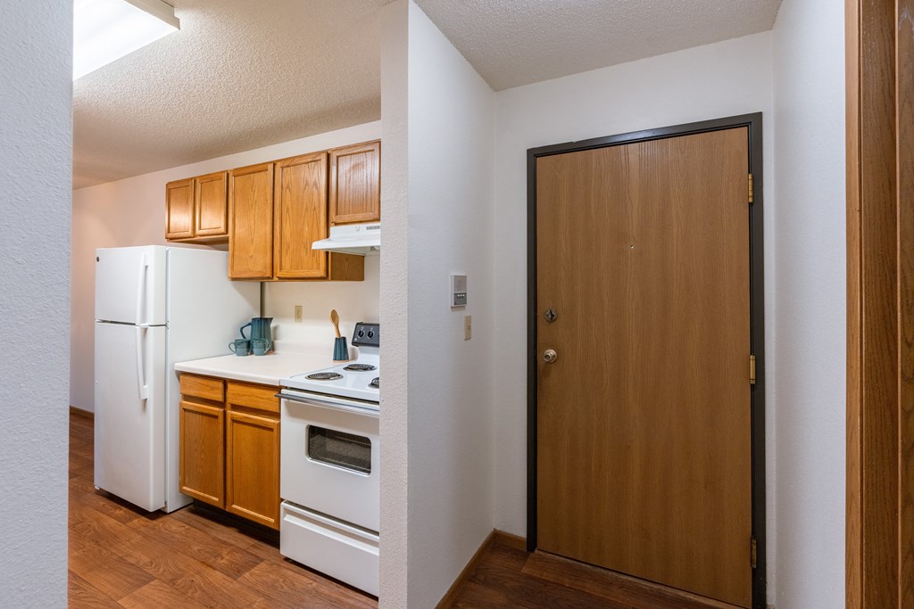 a kitchen with white appliances and a wooden door. Fargo, ND Country Edge Apartments