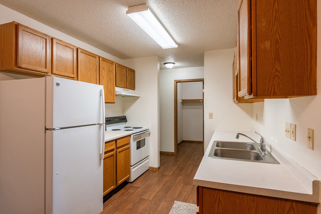 a kitchen with white appliances and wooden cabinets and a refrigerator. Fargo, ND Country Edge Apartments
