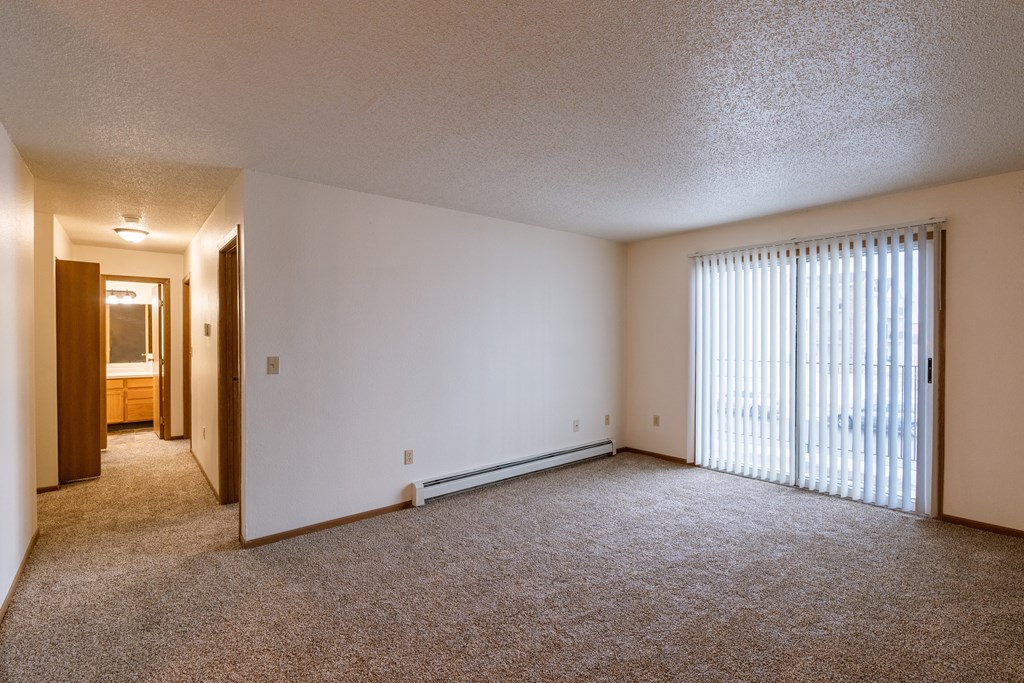the living room of an apartment with a large window and carpeting. Fargo, ND Country Edge Apartments