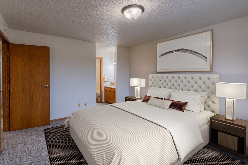 a bedroom with a large bed and a door to a bathroom. Fargo, ND Crescent Park Apartments