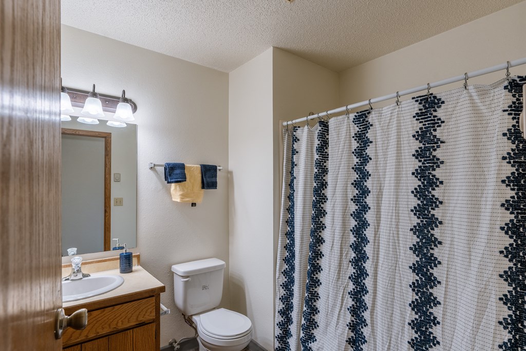 a bathroom with a shower and a toilet and a sink. Fargo, ND Crescent Park Apartments