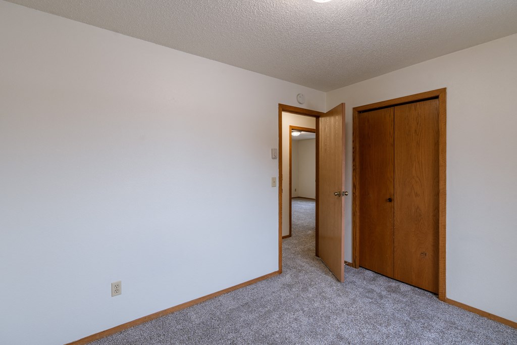a bedroom with a closet and a door to a hallway. Fargo, ND Crescent Park Apartments