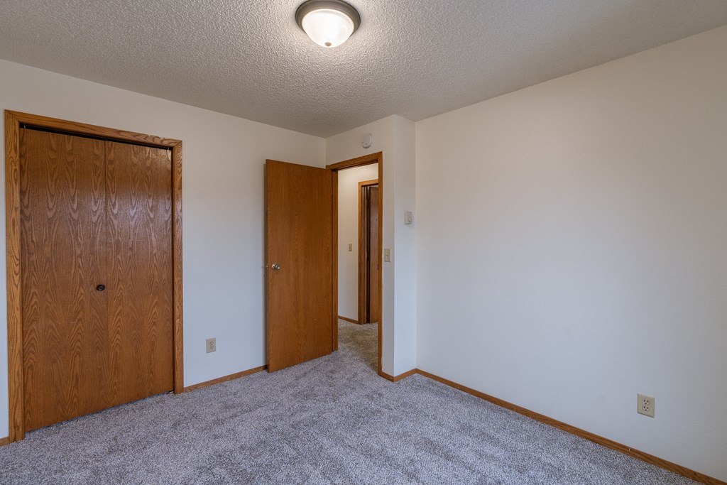 a bedroom with carpet and a door to a hallway. Fargo, ND Crescent Park Apartments