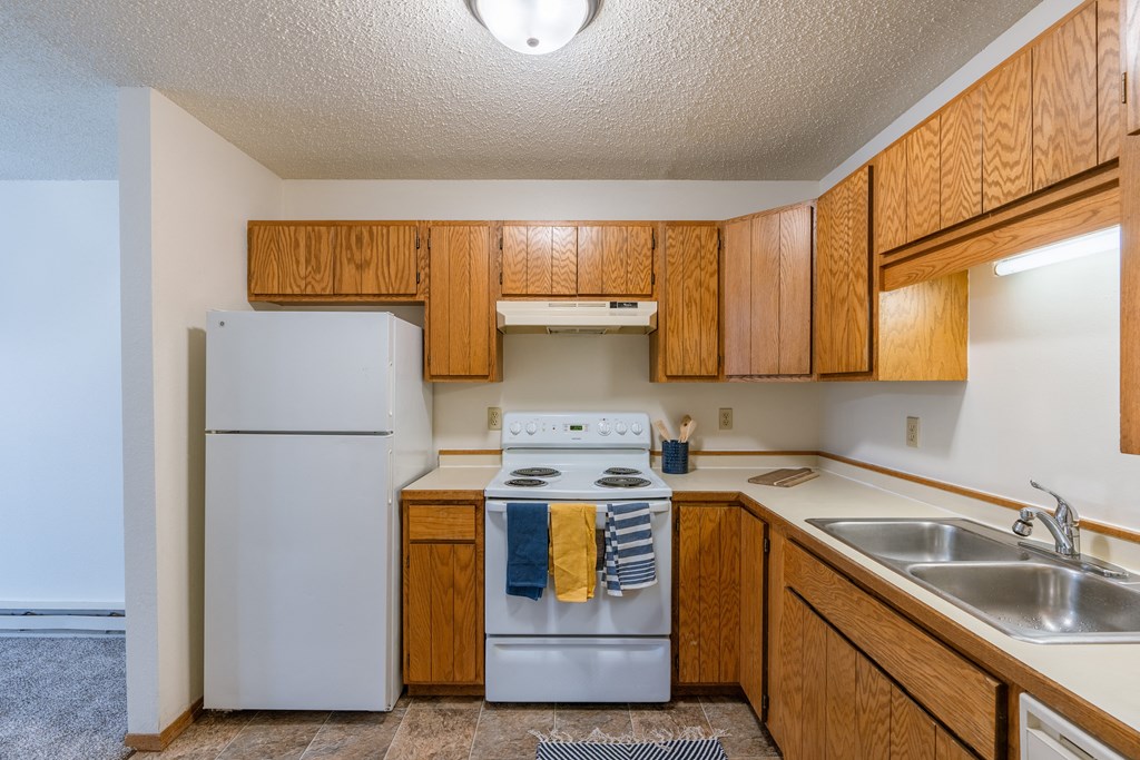 a kitchen with white appliances and wooden cabinets and a white refrigerator. Fargo, ND Crescent Park Apartments