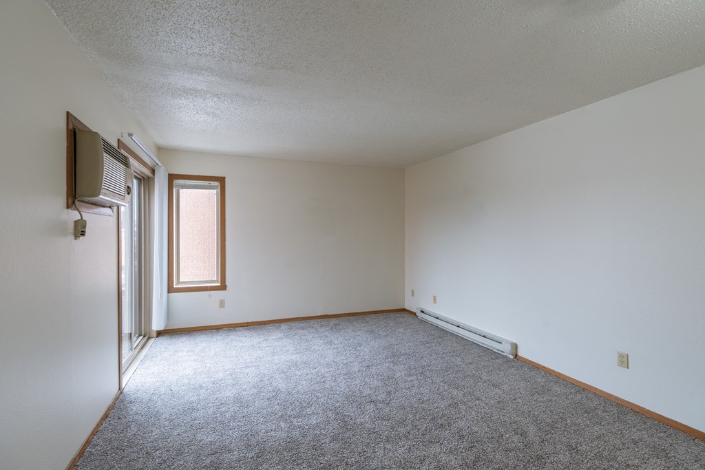 an empty living room with carpet and a window. Fargo, ND Crescent Park Apartments