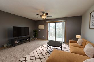 Fargo, ND Danbury Apartments. a living room with a ceiling fan and a sliding glass door to a balcony