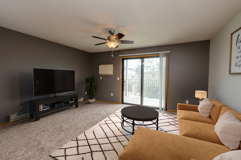 Fargo, ND Danbury Apartments. a living room with a ceiling fan and a sliding glass door to a balcony