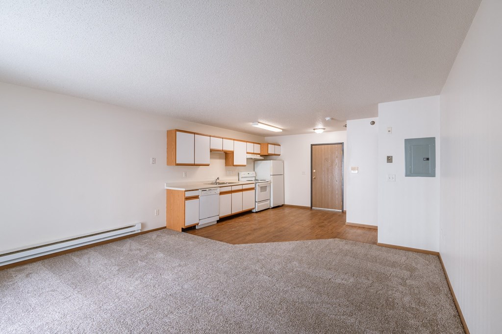 the living room and kitchen of an apartment with a carpeted floor. Fargo, ND Eagle Run Apartments