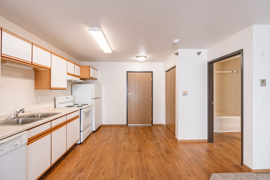 a kitchen with white appliances and wood flooring and a door to the bathroom. Fargo, ND Eagle Run Apartments