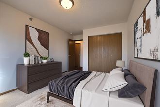 a bedroom with a bed and a dresser and a door to a bathroom. Fargo, ND Eagle Run Apartments