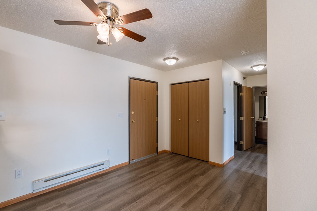 an empty living room with a ceiling fan and a closet. Fargo, ND Eagle Run Apartments