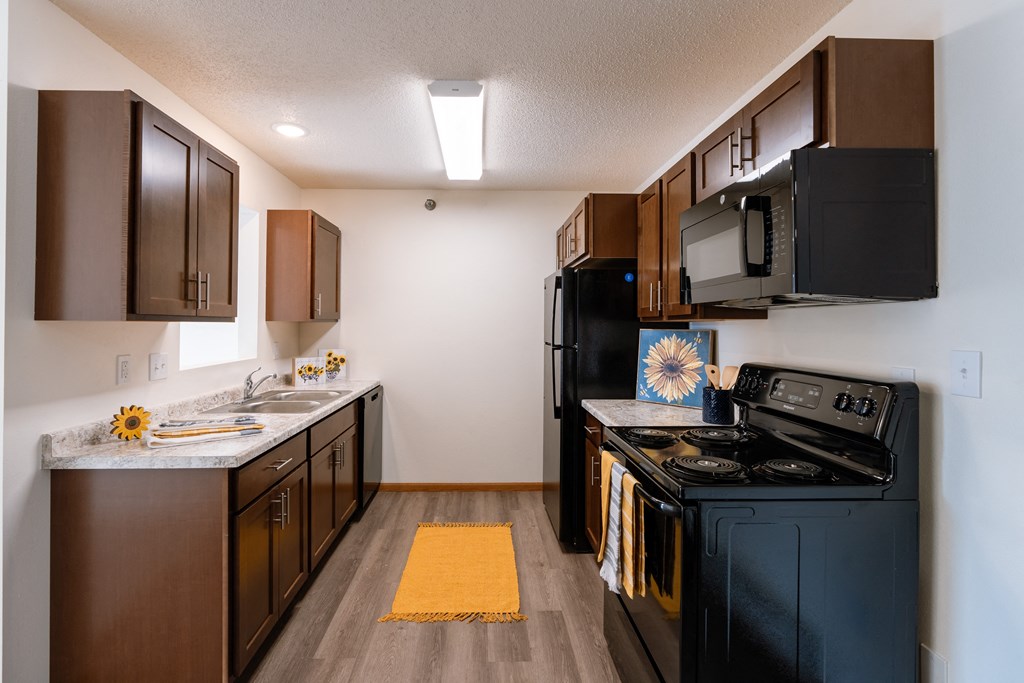 a kitchen with black appliances and brown cabinets and a black stove. Fargo, ND Eagle Run Apartments