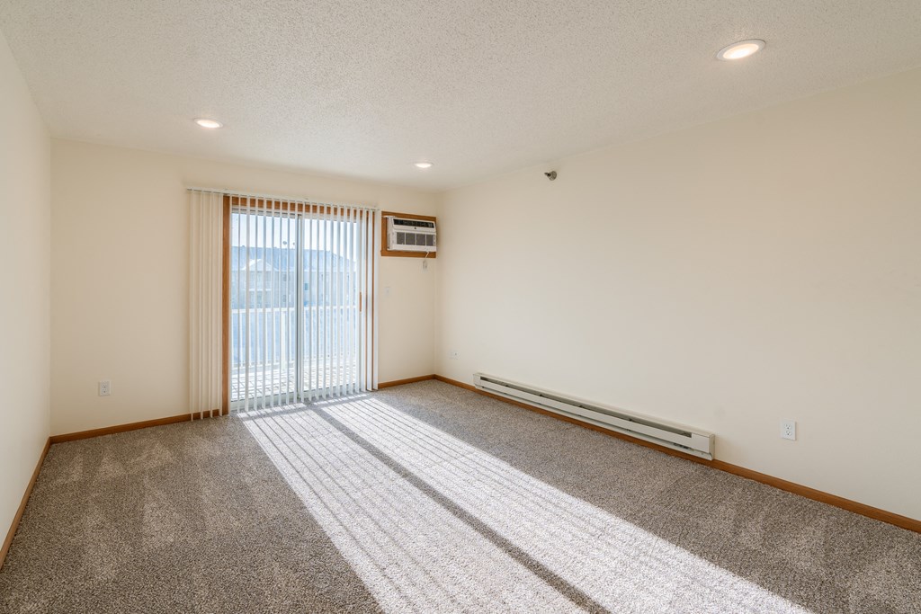 the living room of an apartment with carpet and a sliding glass door. Fargo, ND Eagle Run Apartments