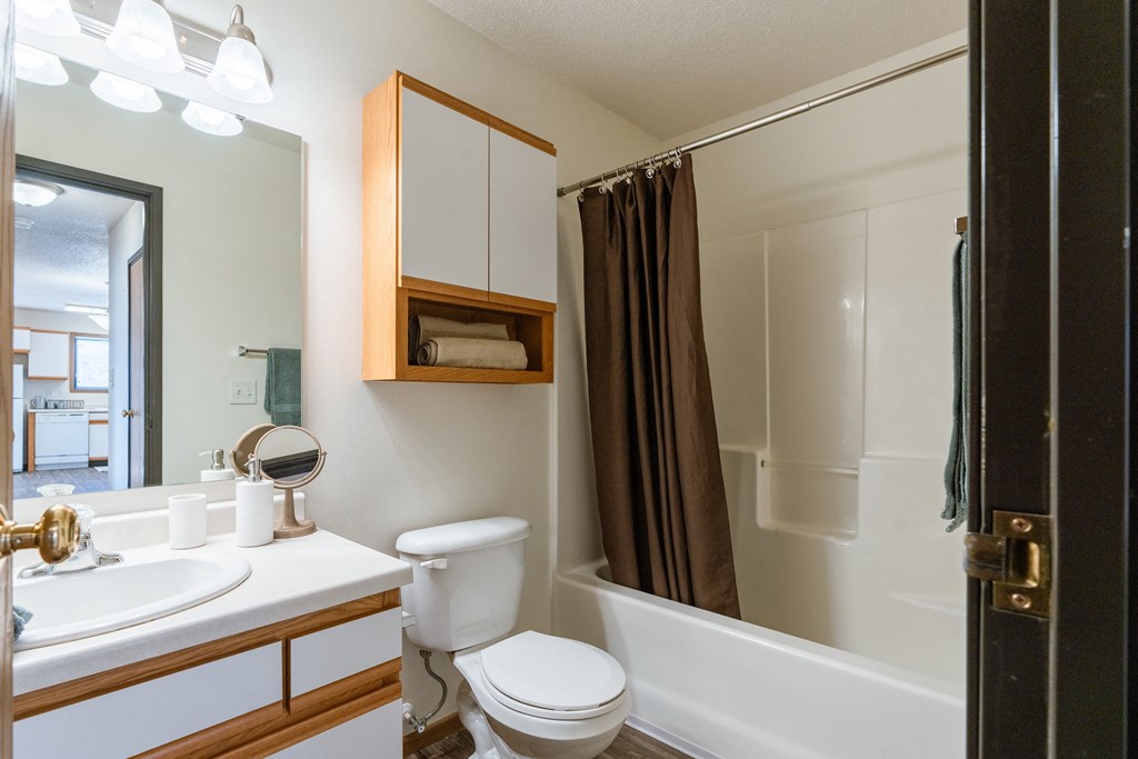 a bathroom with a shower toilet and sink and a mirror. Fargo, ND Eagle Run Apartments