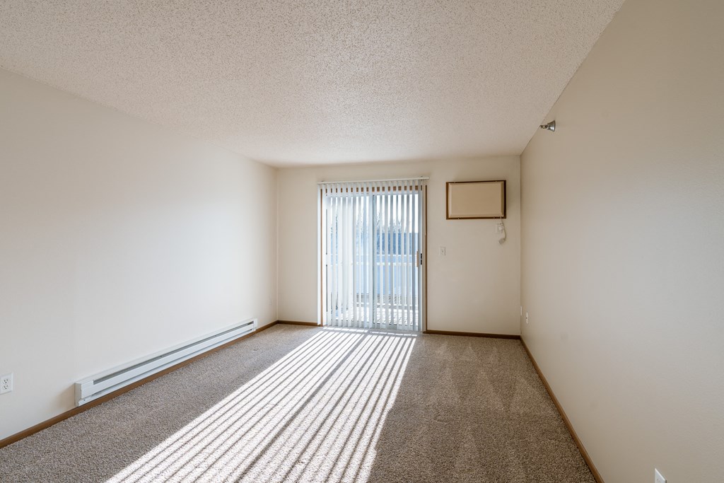an empty living room with a sliding glass door to a balcony. Fargo, ND Eagle Run Apartments