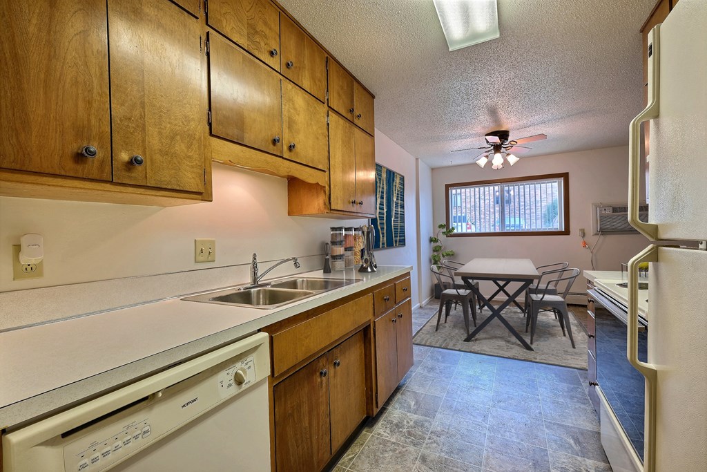 A kitchen with wooden cabinets and a white dishwasher. Fargo, ND Emerald Apartments