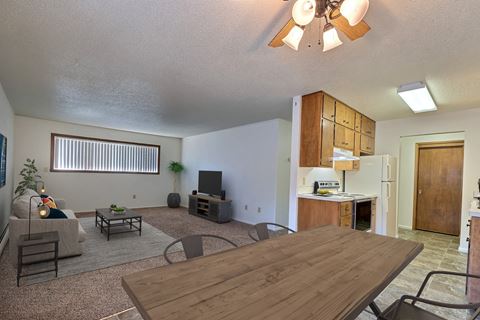 a living room with a wooden table and chairs and a kitchen with a refrigerator and stove. Fargo, ND Emerald Apartments