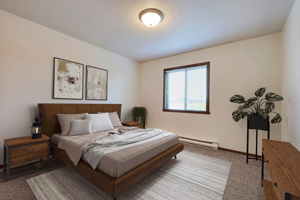 A bedroom with a large bed and a window. Fargo, ND Flagstone Apartments.