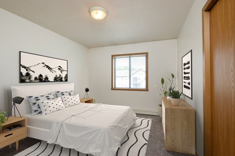 Fargo, ND Flickertail Apartments. a bedroom with a white bed and a wooden dresser with a plant on it