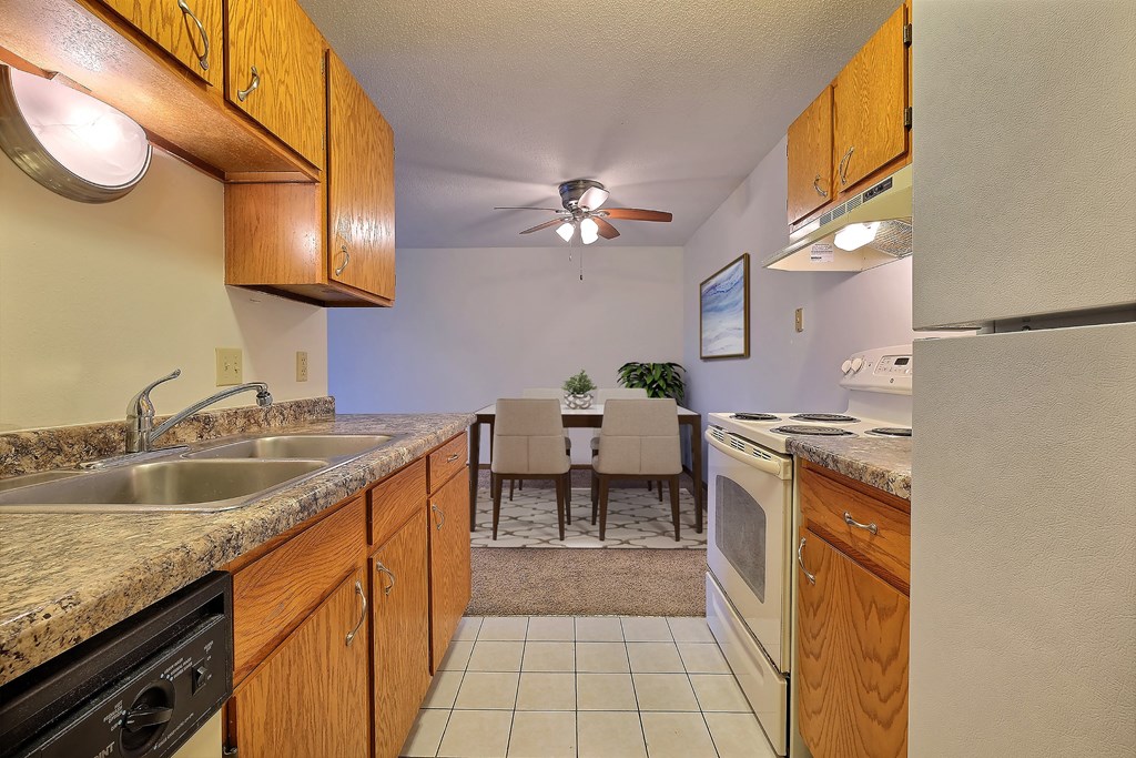a kitchen with wooden cabinets and a dining room in the background. Fargo, ND France Apartments