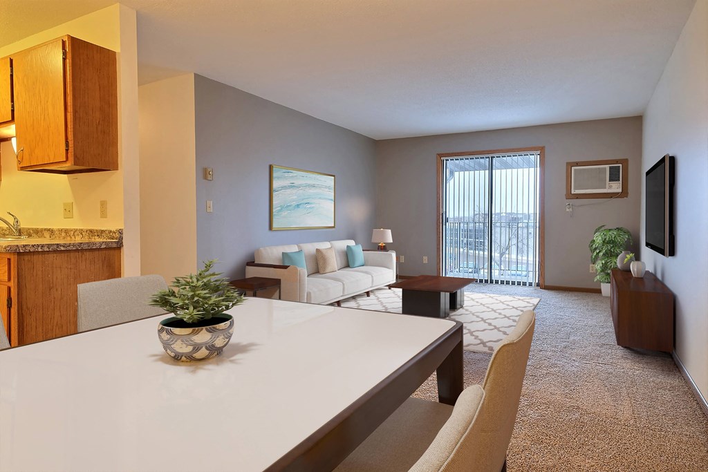 a living room with a white table and chairs and a sliding glass door leading to a balcony. Fargo, ND France Apartments