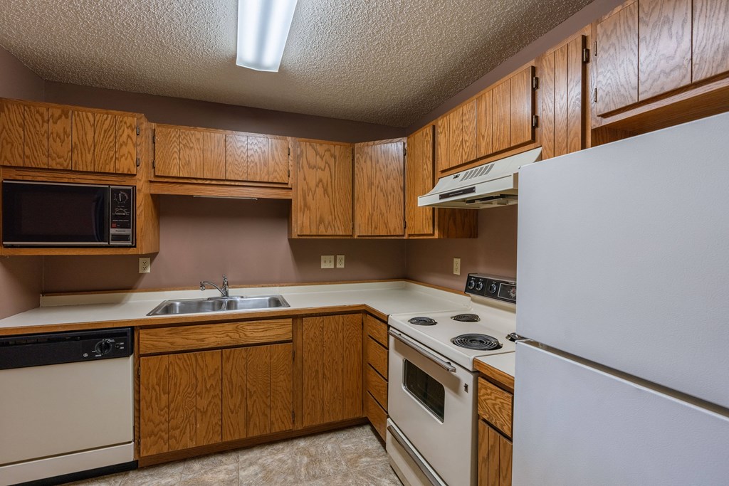 an empty kitchen with white appliances and wooden cabinets. Fargo, ND Galleria Apartments