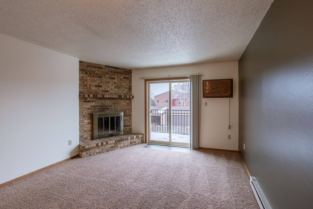 an empty living room with a fireplace and a door to a balcony. Fargo, ND Galleria Apartments