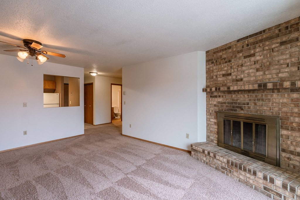 an empty living room with a brick fireplace and a ceiling fan. Fargo, ND Galleria Apartments