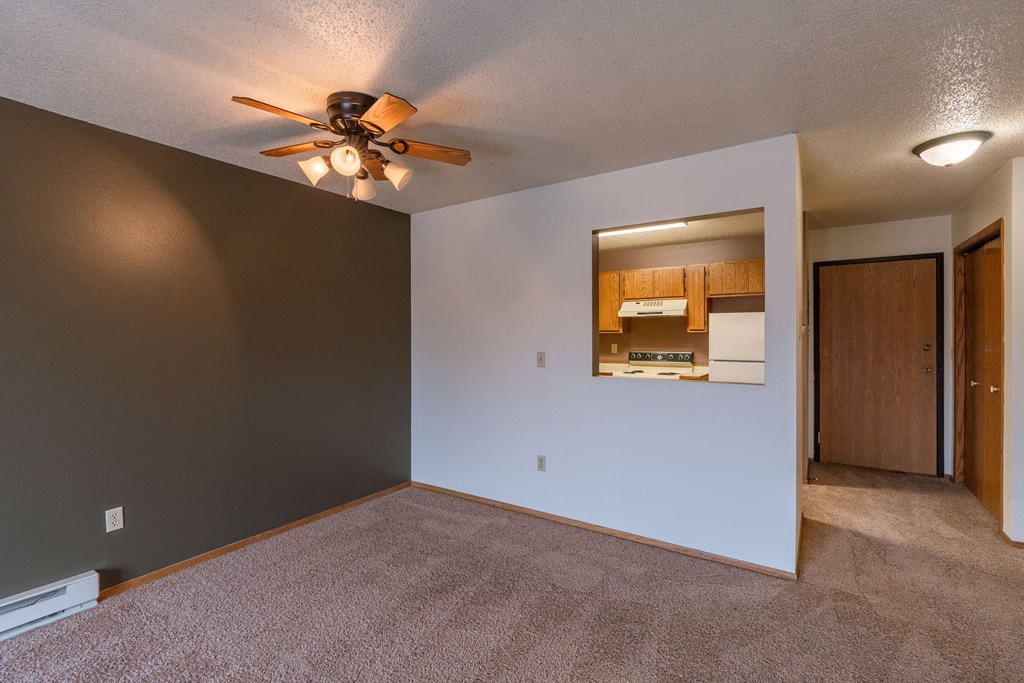 an empty living room with a ceiling fan and a kitchen. Fargo, ND Galleria Apartments