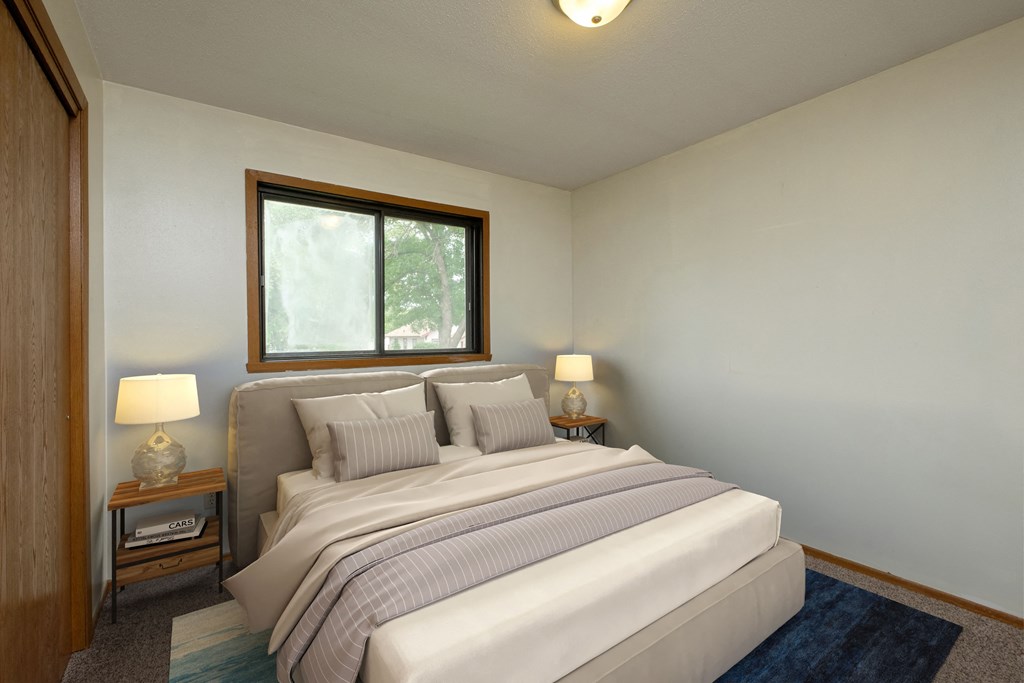 Fargo, ND Gemstone Apartments. A bedroom with a bed and two night stands and a window.