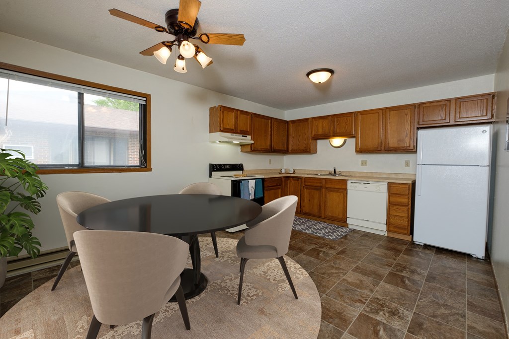 Fargo, ND Gemstone Apartments. a dining area with a table and chairs and a kitchen with a refrigerator and dishwasher. A window fills the room with bright natural light